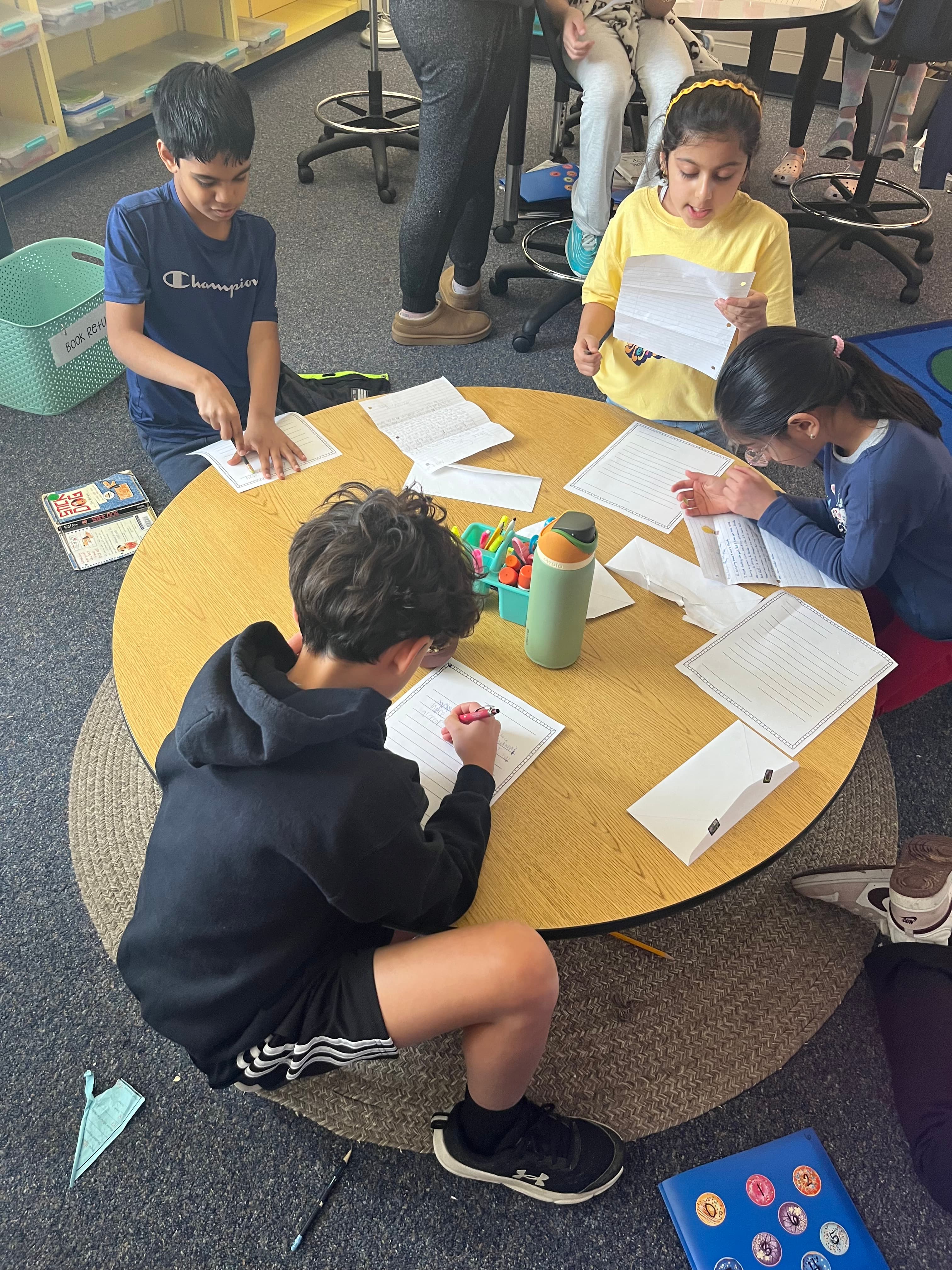 Kids at round table writing letters overhead view