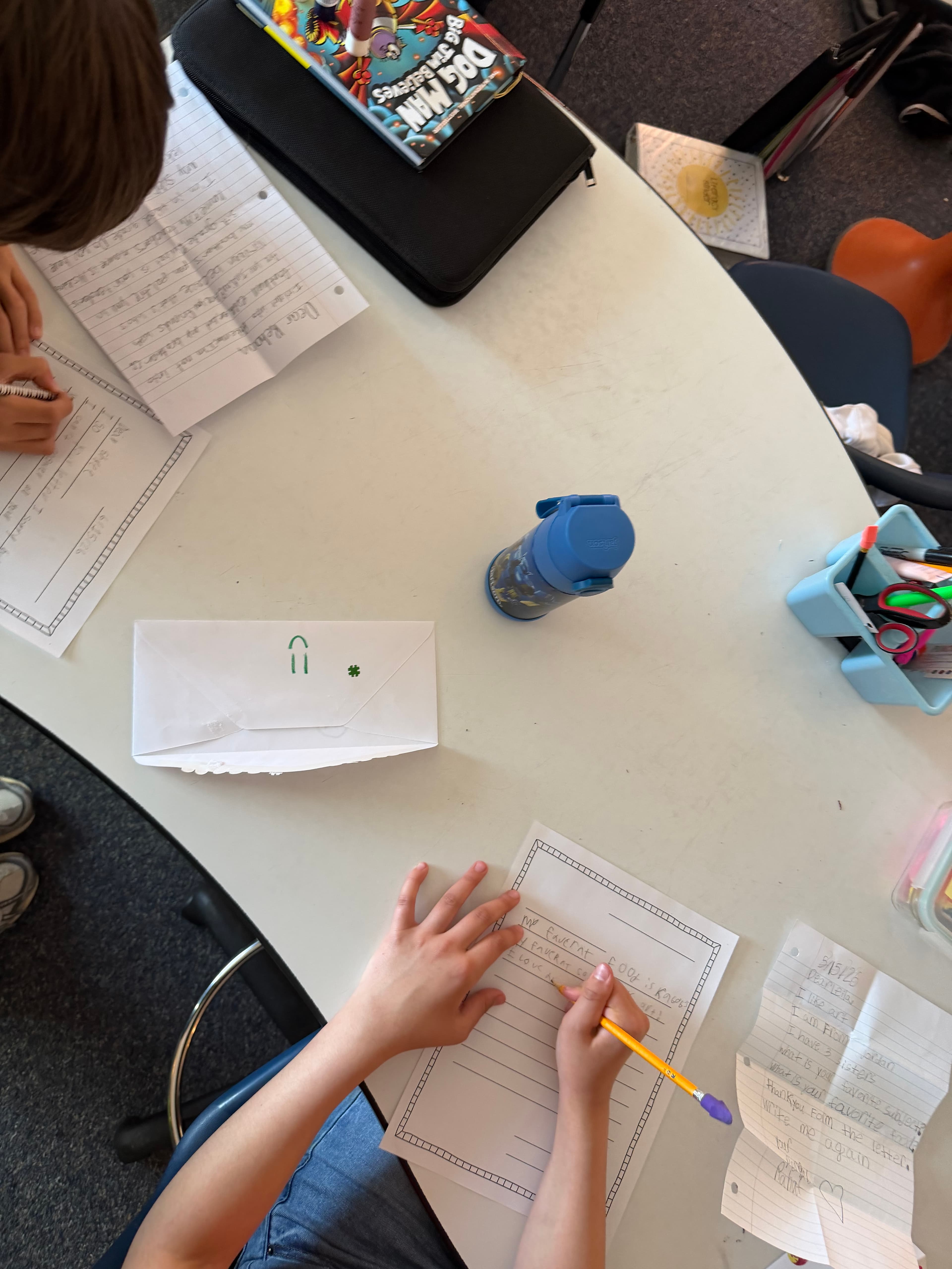 Students writing letters at a round table with a sealed envelope in the middle